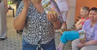 Prijímateľka sociálnej služby s balíčkom chrumiek počas príjemného posedenia a oddychu v areáli zariadenia